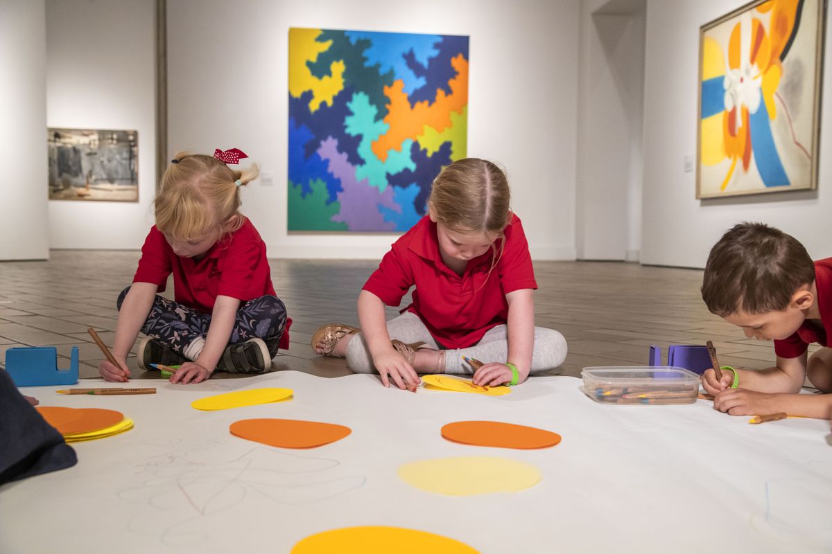 A group of primary school children sit on the gallery floor and work together on an artwork