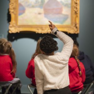 Photograph of school children sitting in front of painting with arms raised to answer question