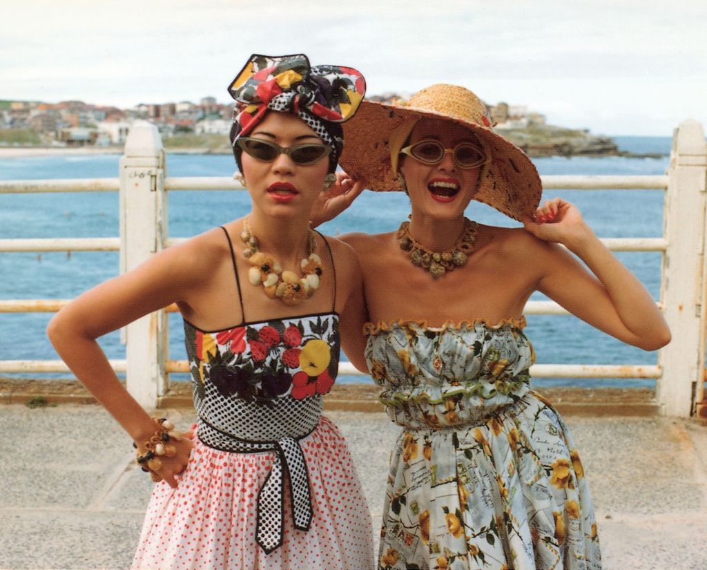 Two women wearing glamorous clothes, hats and jewellery pose together