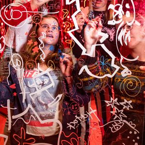 Young women are standing behind a piece of clear perspex, using markers to draw and write on it