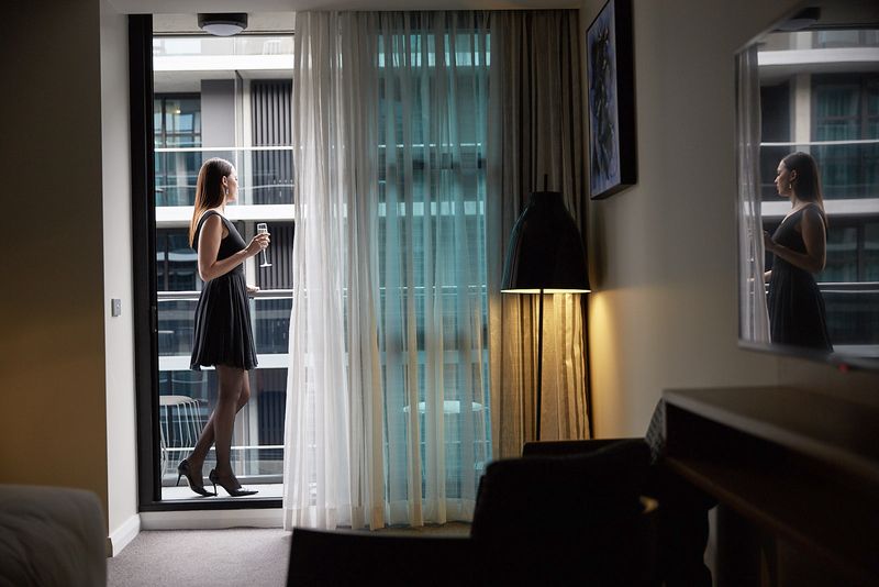 Woman in a black dress standing on the balcony of a hotel room, holding a glass of champagne