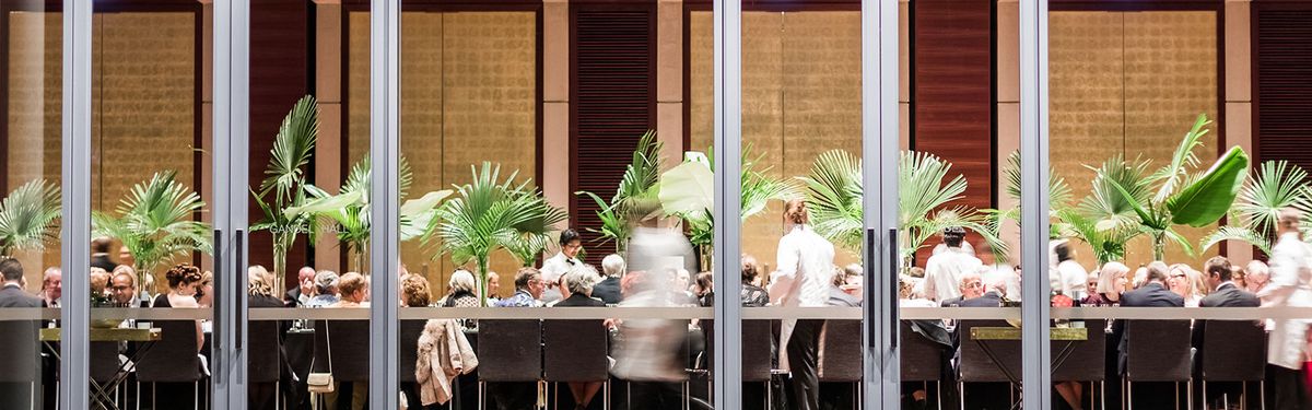 Photo of a large gathering at a forma event of people sitting down eating and drinking being served by wait staff