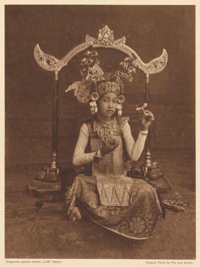 A young Balinese dancer sits while holding a pose, surrounded by a decorative frame