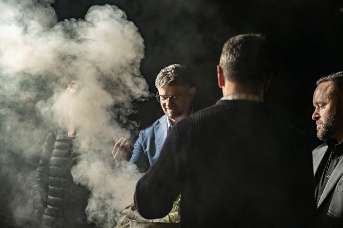 One man is holding a metal bucket that is emitting plumes of smoke from native leaves. Three other people are gathered around taking part in the smoking ceremony.