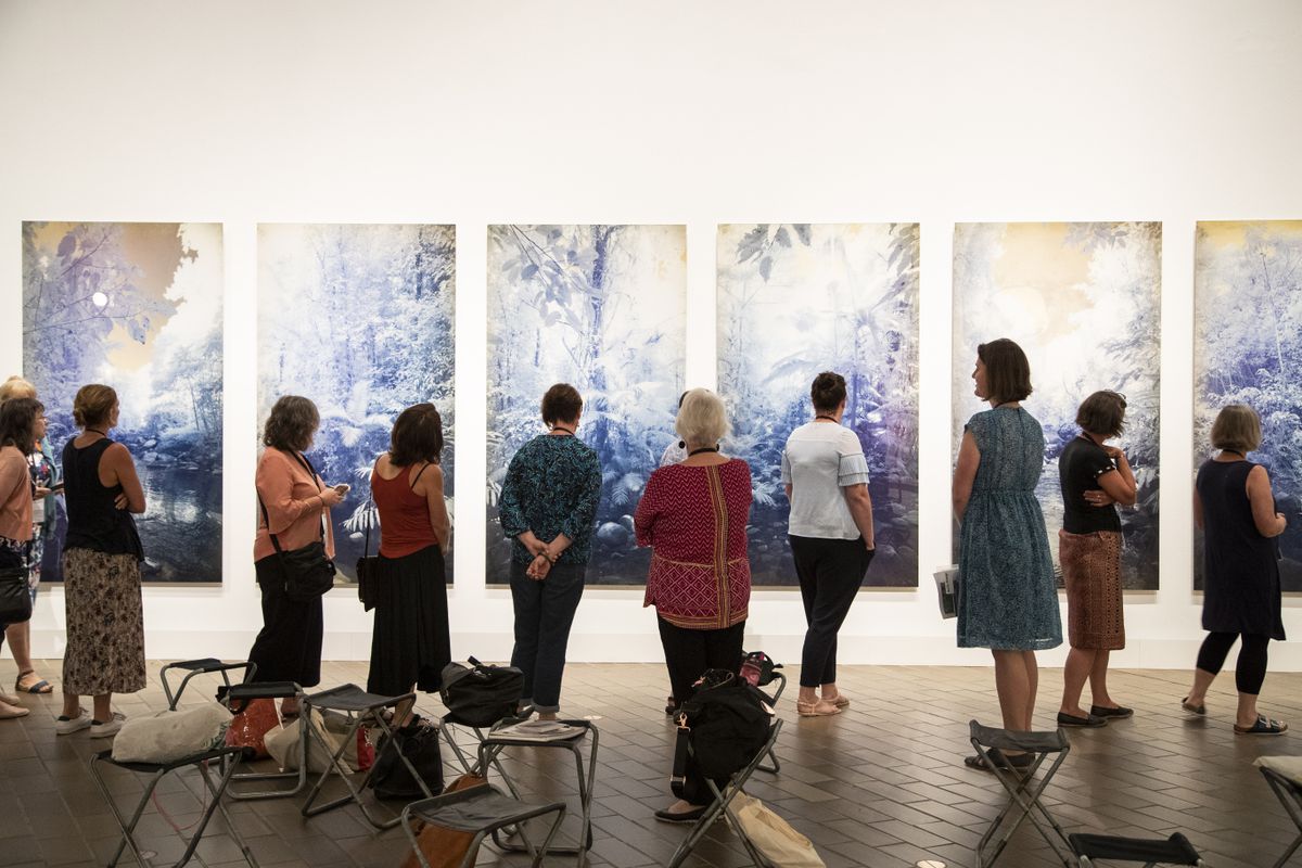 a group of people are standing looking at a multi-panelled work of art