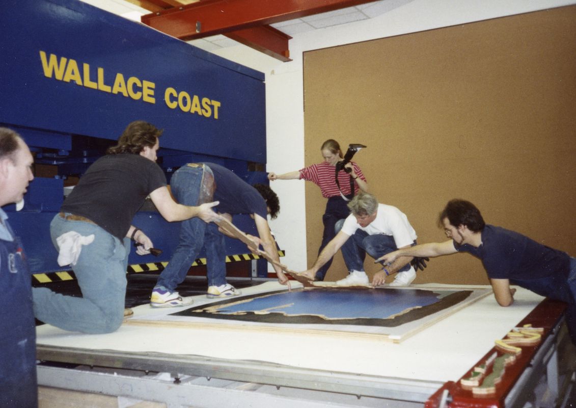 A team of people surround an artwork on the floor with a sign to the left saying "Wallace Coast"