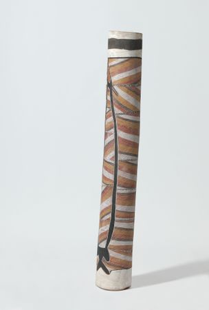 A shorter, wide pole with a slight right lean. Traditional ochre, yellow, white and black painting with repeating stripe pattern