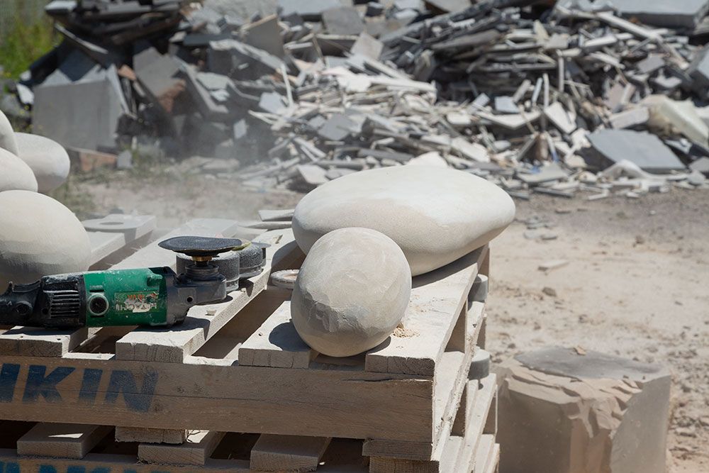 Two carved rocks sit on a wooden pallet next to an angle grinder