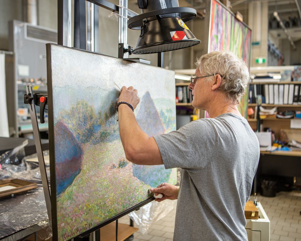 a man using cleaning tools to perform conservation on a painting in a laboratory
