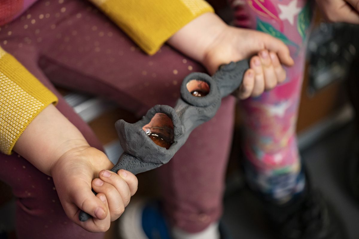 a pair of hands, belonging to a small child, are holding a black ceramic object