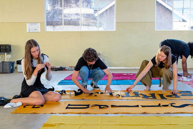 Four people sitting on the floor working on a piece of orange fabric