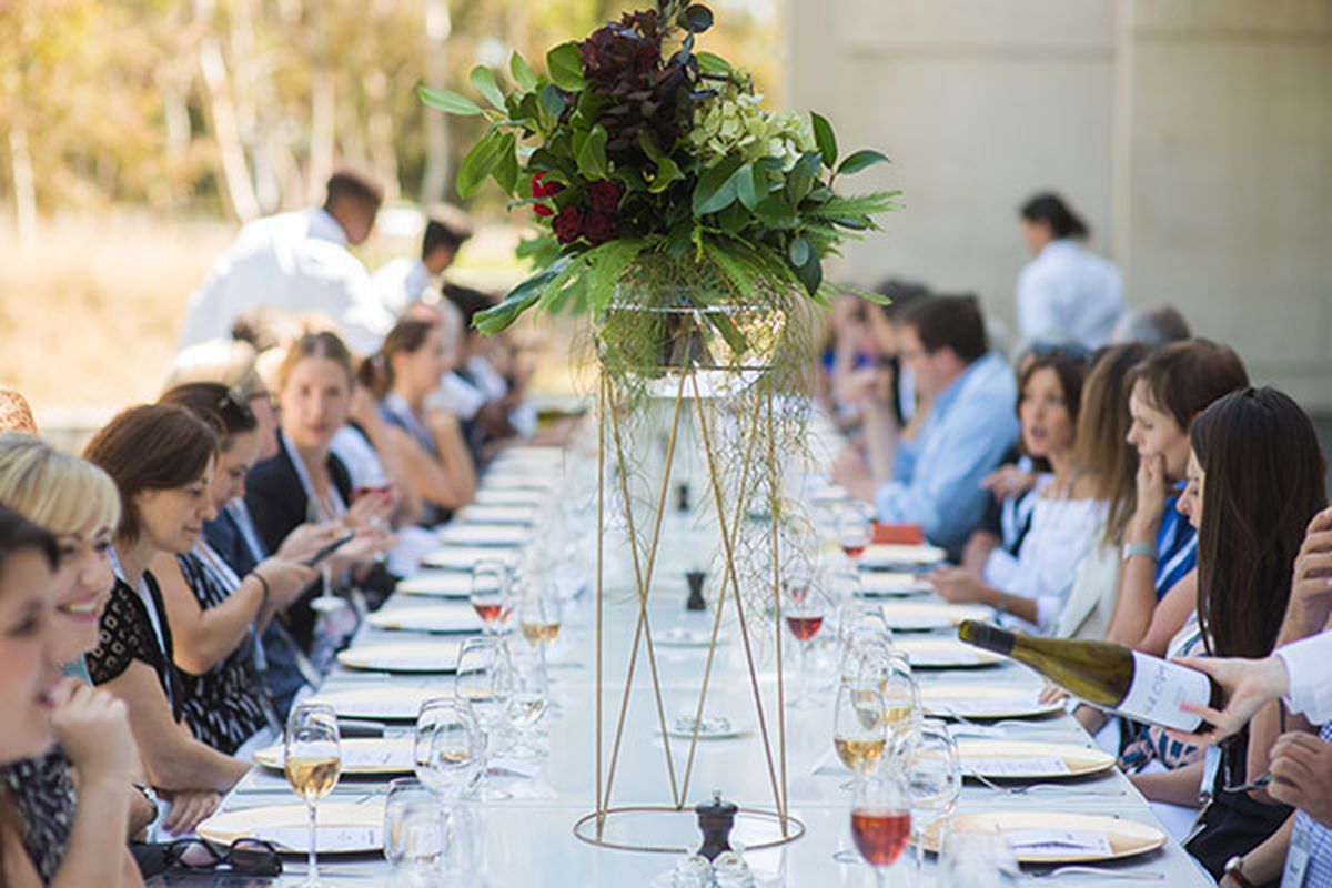 Group of people sitting at a long table with table decorations, and plates and wine glasses