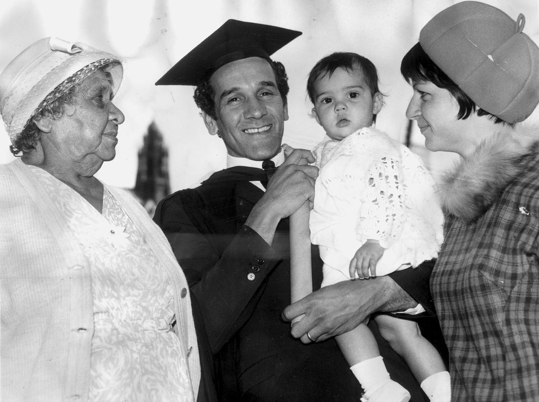 Photograph of an in graduation regalia holding a baby with two women either side