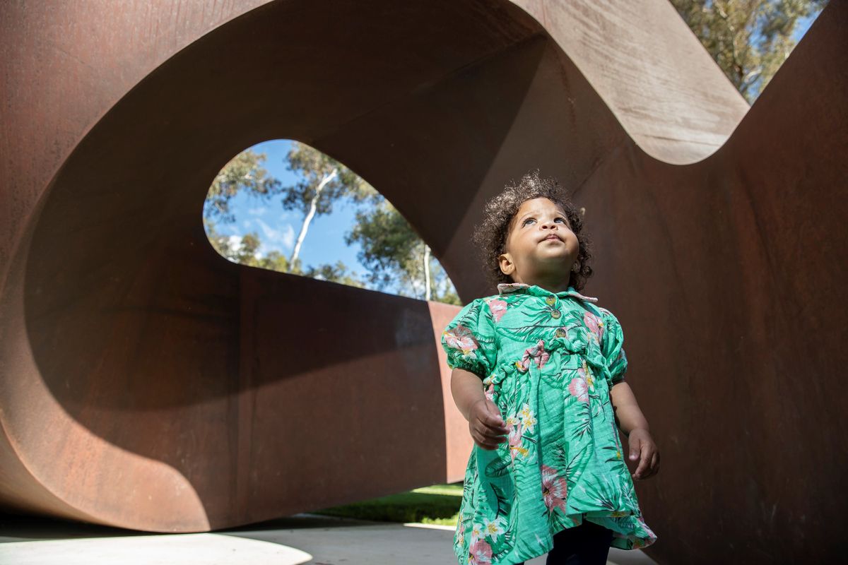 A toddler stands inside a large metal twisting sculpture