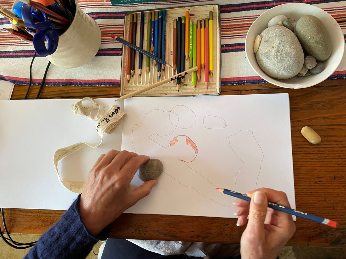 A woman's hands holding an orange pencil which she has used to shade areas on a blank sheet of paper