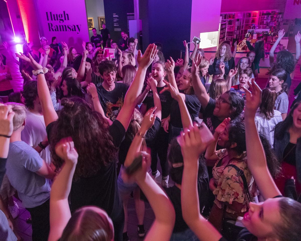a group of young people are dancing with their arms up in the air under coloured purple lighting