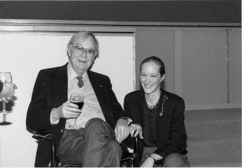 A photograph of a man sitting in a chair holding a glass of wine while a woman crouches next to him