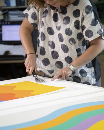 A conservator stands at table working on two brightly-coloured works of art