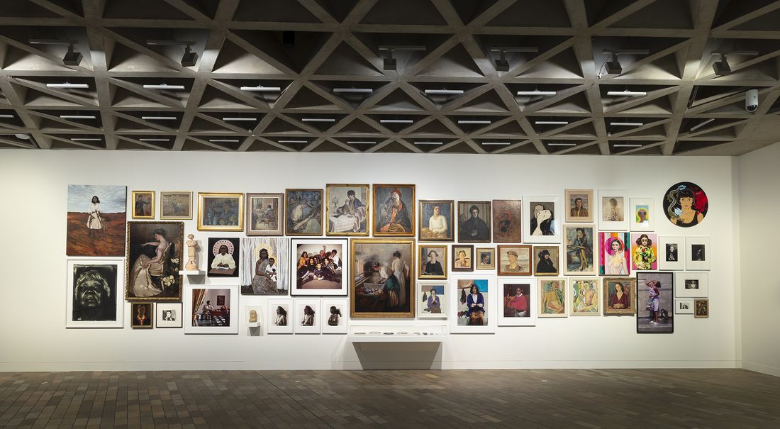 A large number of portraits are hanging salon style on a long gallery wall