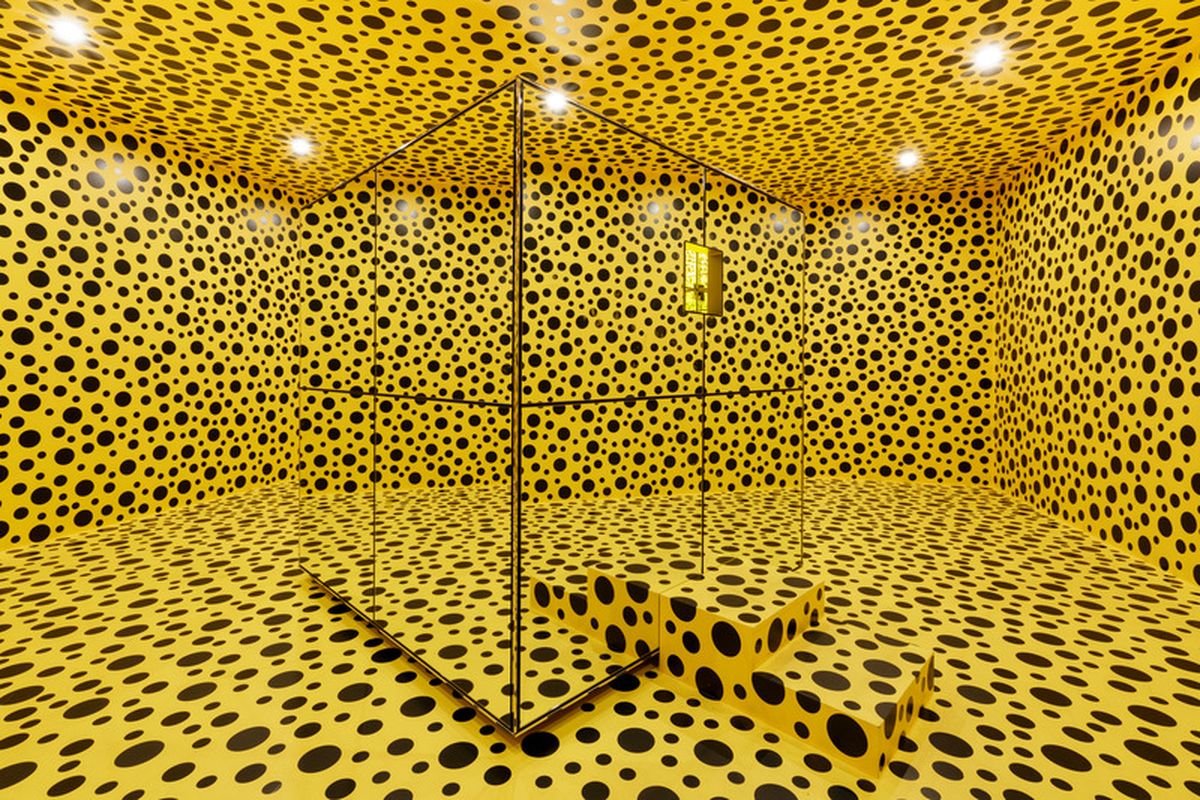 A small bright yellow room with black dots and a mirrored box in the middle