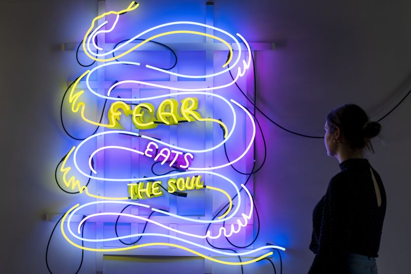 Photograph of woman looking at neon art in dark gallery