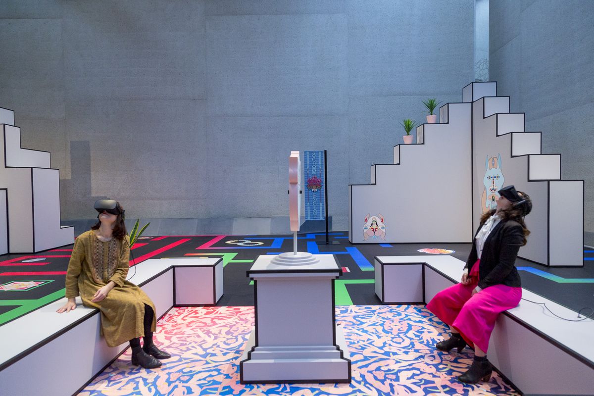 Two people wearing virtual reality headsets sit opposite each other in an art installation