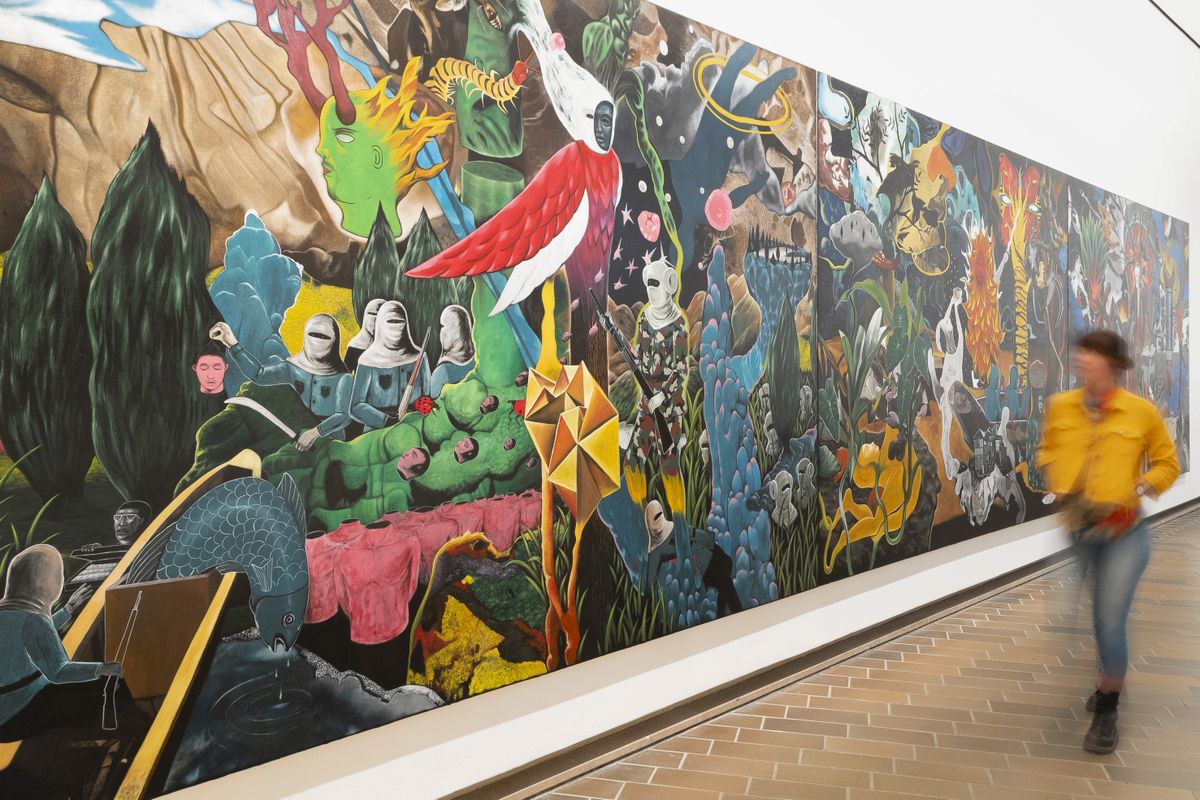 Photograph of women walking in front of large colourful painting by Rodel Tapaya.