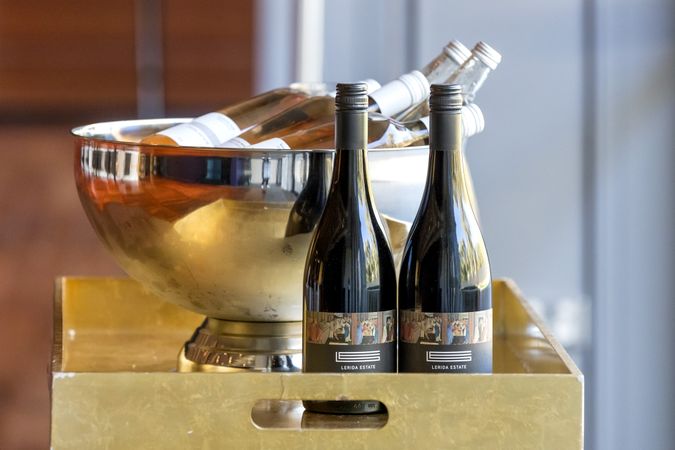 Two bottles of red wine stand on a tray in front of a cooler bowl filled with bottles of rose