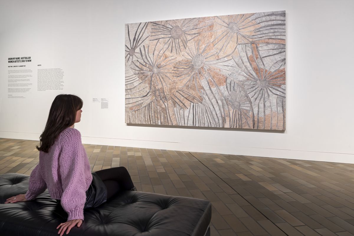Photograph of woman sitting on black seat looking at artwork