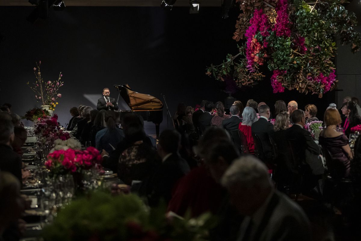 Photograph of gala dinner with guests seated amongst flowers and speaker in distance