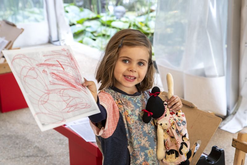 Photograph of child by an easel, showing off artwork