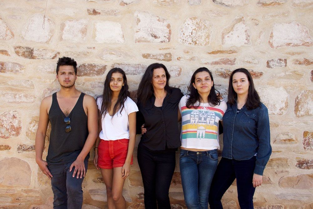 Photograph of five people standing in a row against a brick wall