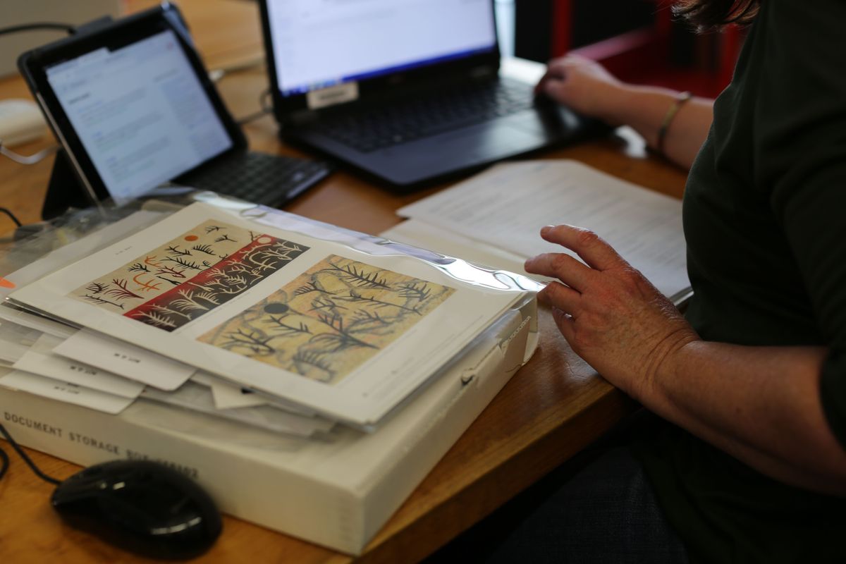 Photograph of woman seated at table with laptop and archival material surrounding her