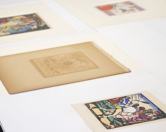 a number of small works of art on paper are laid out on a table for conservation treatment