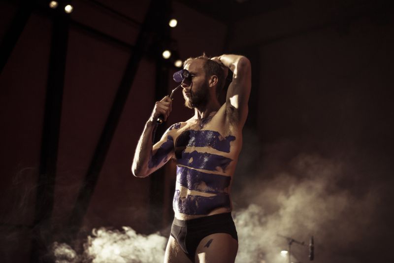 Semi naked bearded man painting purple paint on his body using a paint roller